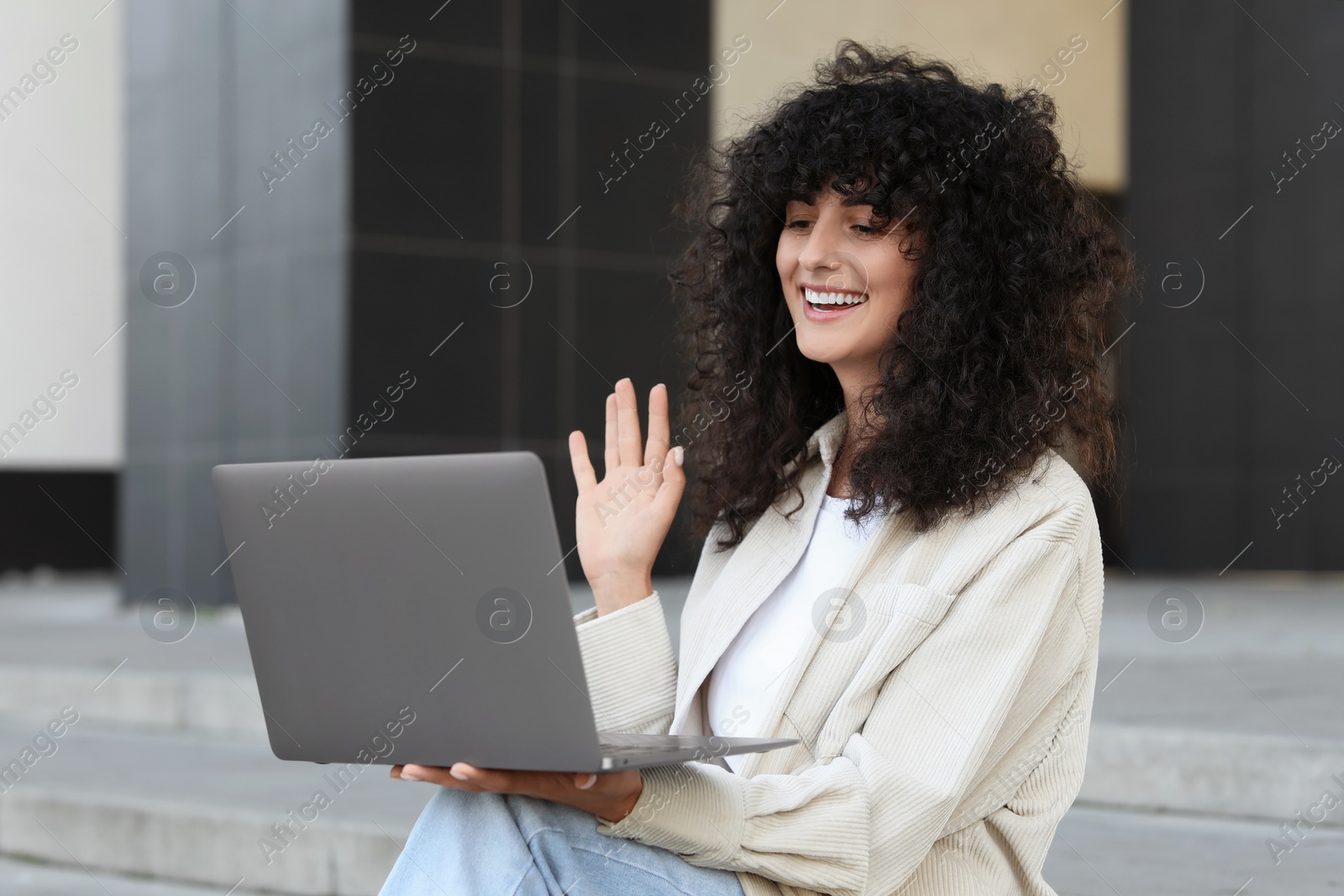 Photo of Happy young woman using modern laptop for video call outdoors