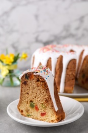 Photo of Piece of glazed Easter cake with sprinkles and candied fruits on grey table
