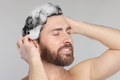 Happy man washing his hair with shampoo on grey background, closeup