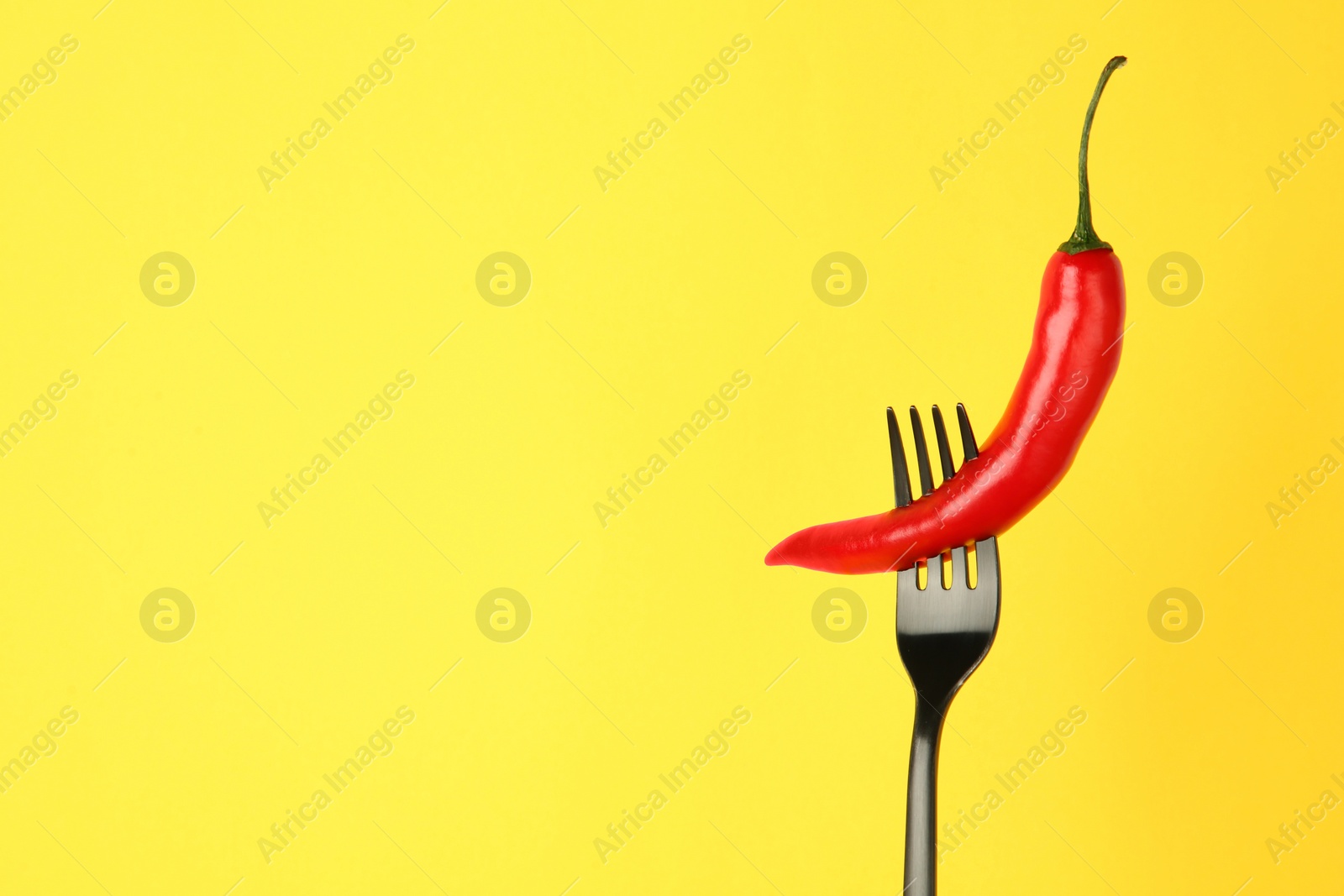 Photo of Fork with chili pepper on yellow background, space for text