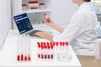 Test tubes with blood samples and scientist working on computer in laboratory