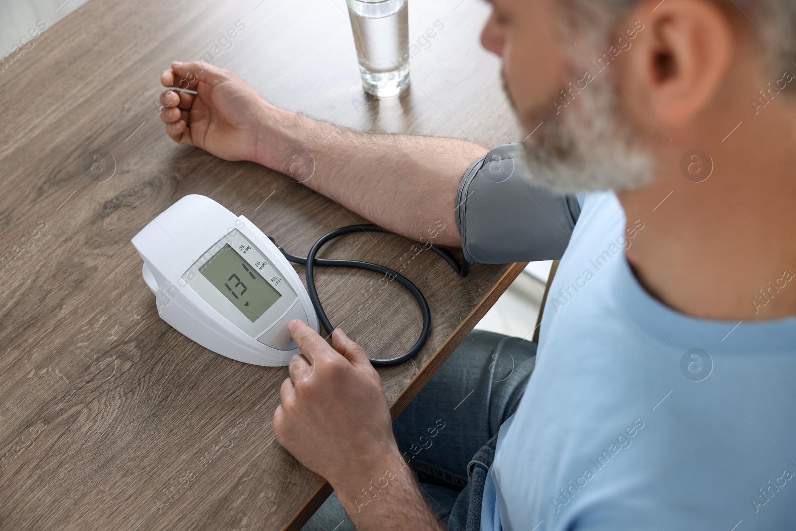 Photo of Man measuring blood pressure at table indoors, closeup