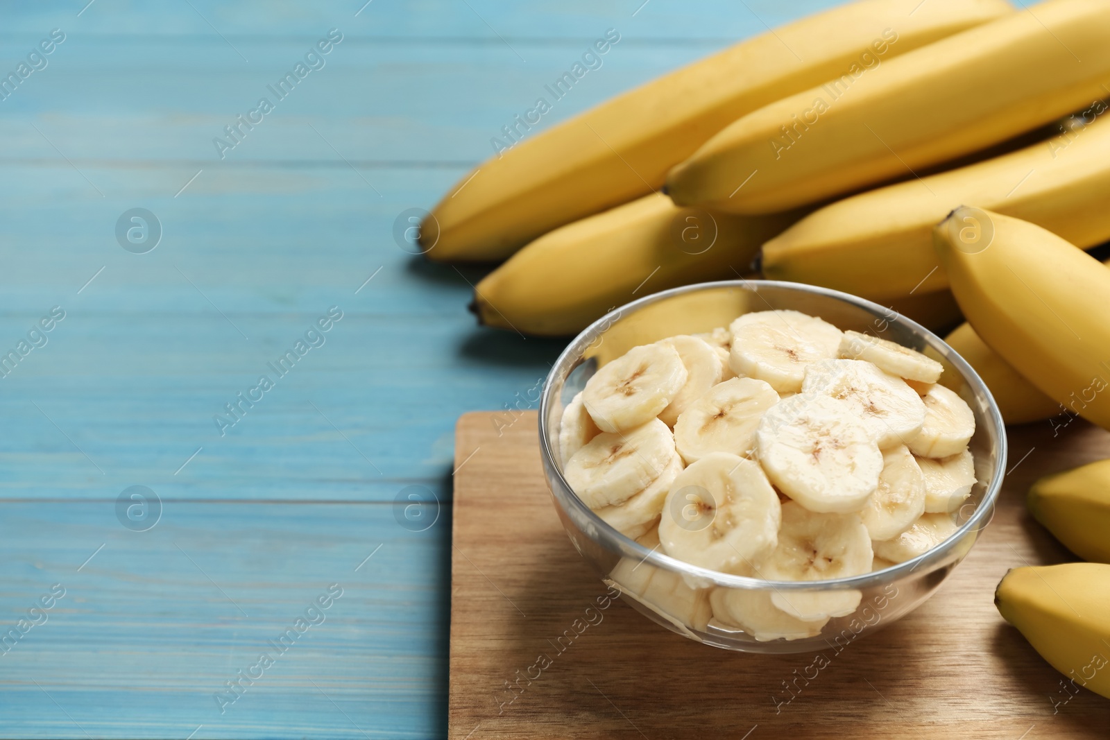 Photo of Bowl with cut bananas near whole fruits on light blue wooden table. Space for text