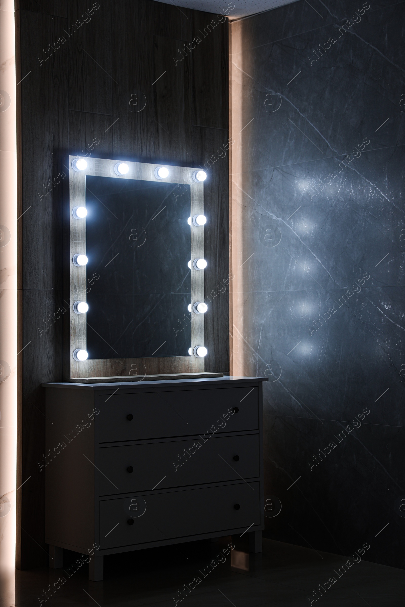 Photo of Modern mirror with light bulbs on grey chest of drawers in room