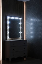 Modern mirror with light bulbs on grey chest of drawers in room