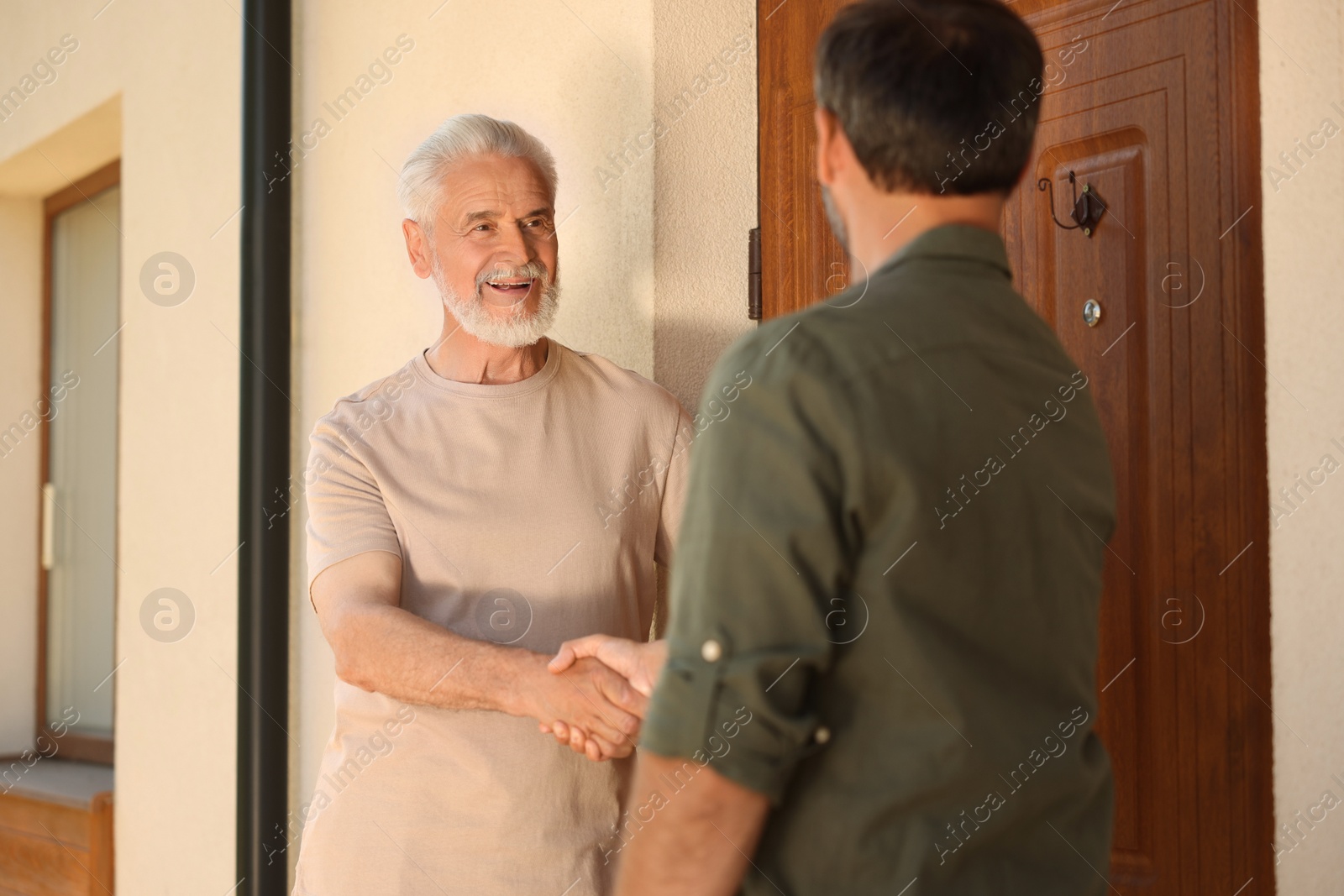 Photo of Friendly relationship with neighbours. Happy men shaking hands near house outdoors