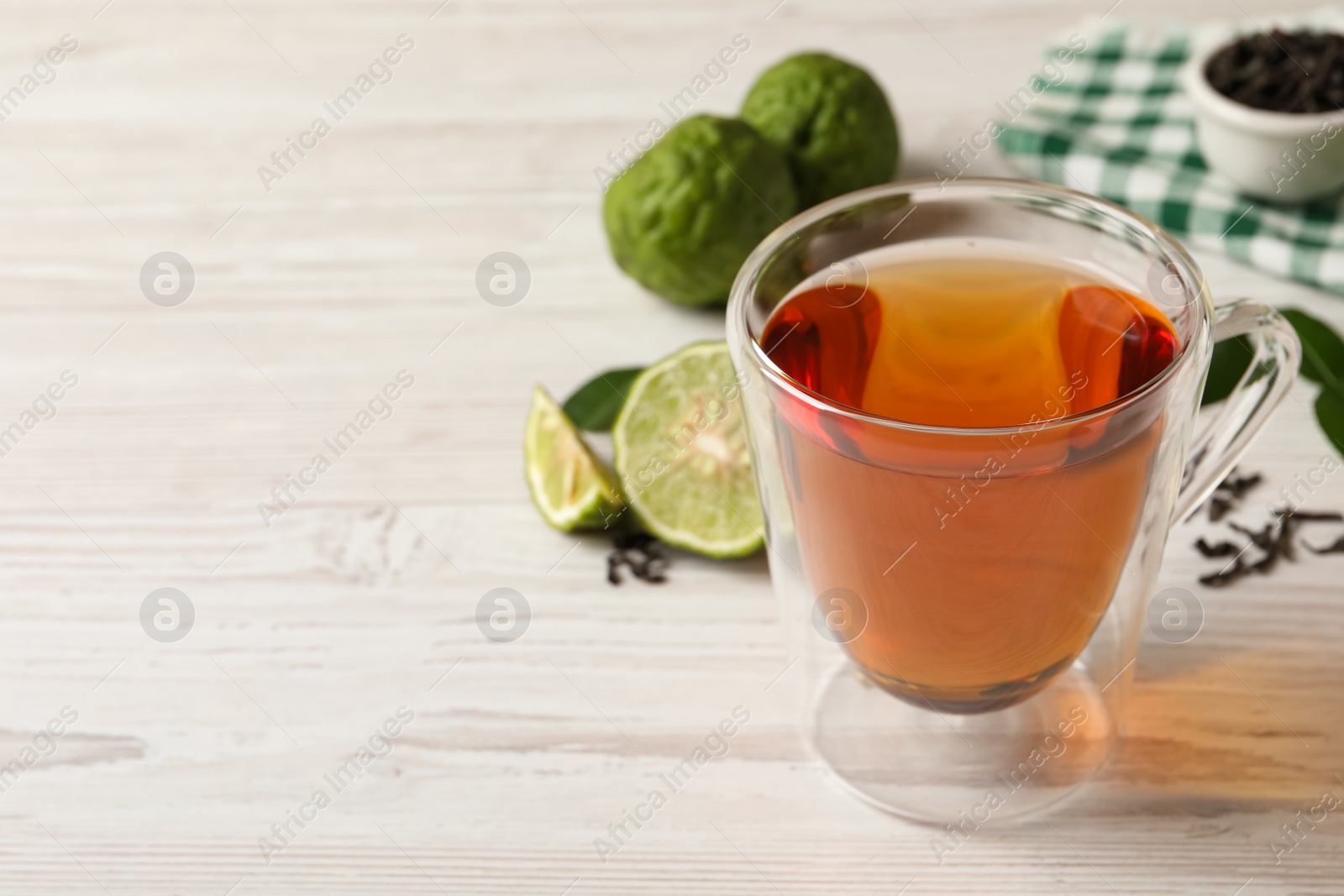 Photo of Glass cup of tasty bergamot tea on white wooden table, space for text