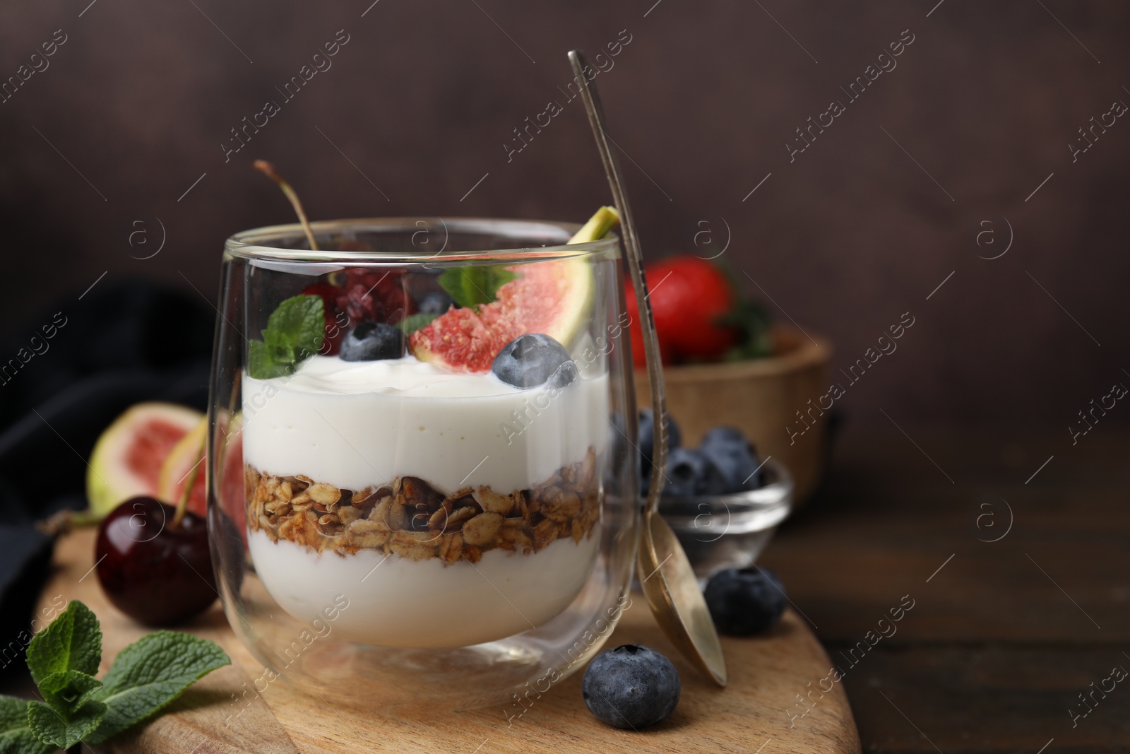 Photo of Glass with yogurt, berries, mint and granola on wooden table, closeup. Space for text