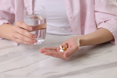 Photo of Woman with vitamin pills and glass of water at table indoors, closeup