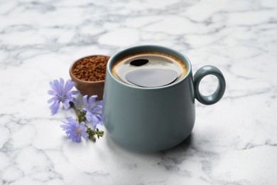 Cup of delicious chicory drink, granules and flowers on white marble table