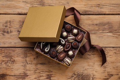 Open box of delicious chocolate candies and brown ribbon on wooden table, flat lay