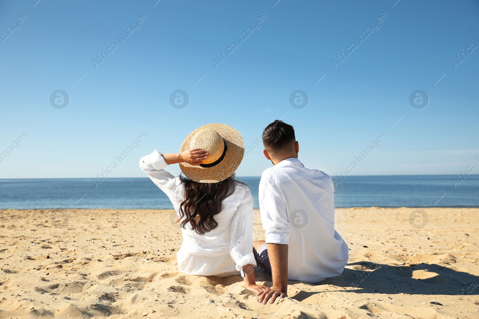 Photo of Young couple on beach near sea, back view. Honeymoon trip