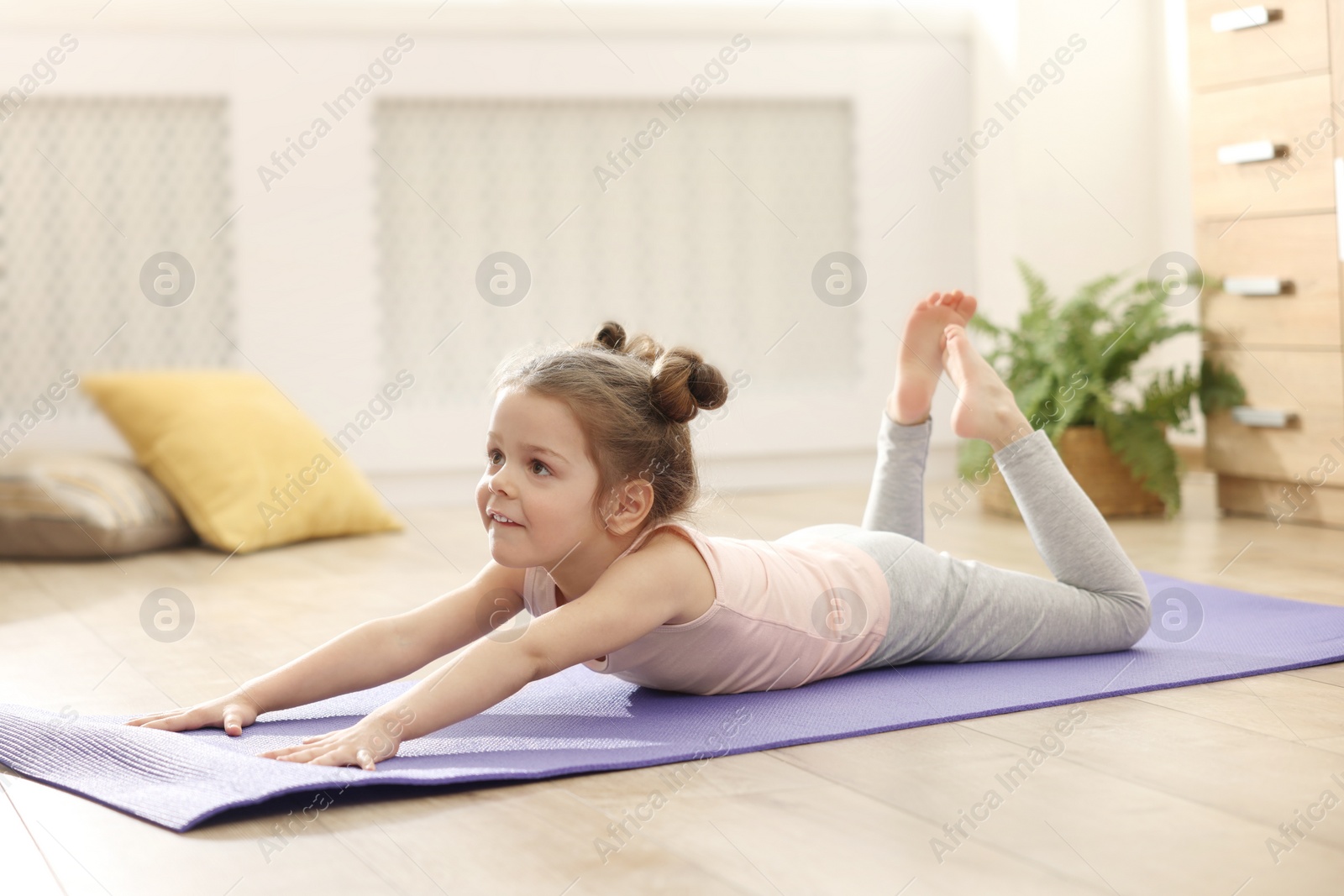 Photo of Little cute girl practicing yoga on mat at home