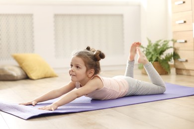 Little cute girl practicing yoga on mat at home