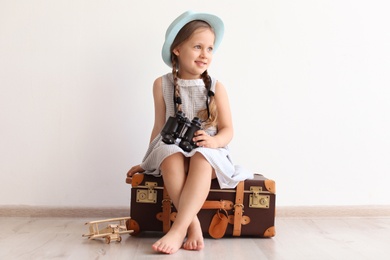 Photo of Adorable little child playing traveler with suitcase indoors