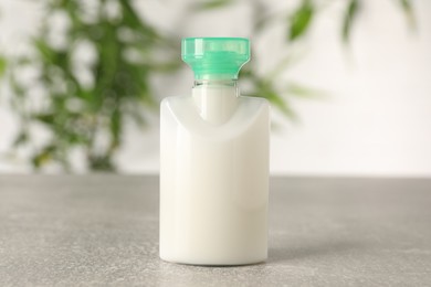 Mini bottle of cosmetic product on light grey table against blurred background, closeup