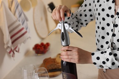 Romantic dinner. Woman opening wine bottle with corkscrew in kitchen, closeup