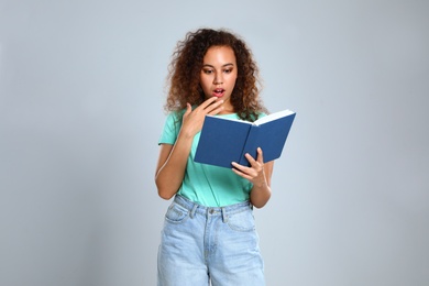 Beautiful African-American young woman reading book on light background