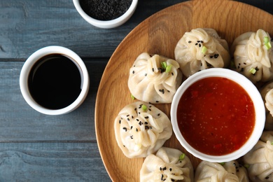 Photo of Tasty baozi dumplings served with sesame seeds and sauces on wooden table, top view