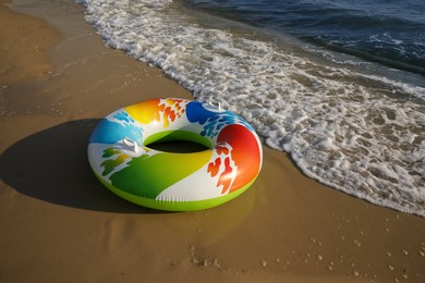 Bright inflatable ring on sandy beach near sea, space for text