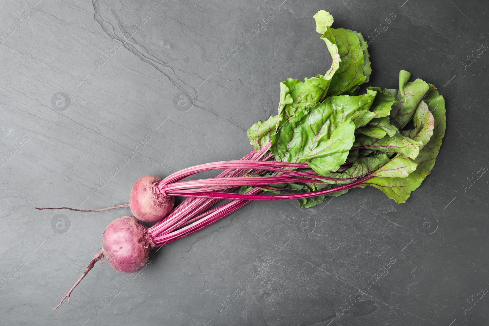 Photo of Raw ripe beets on black slate table, flat lay