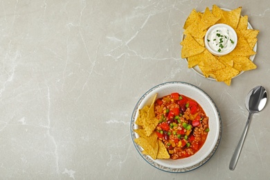 Chili con carne served with sauce and tortilla chips on grey table, top view. Space for text