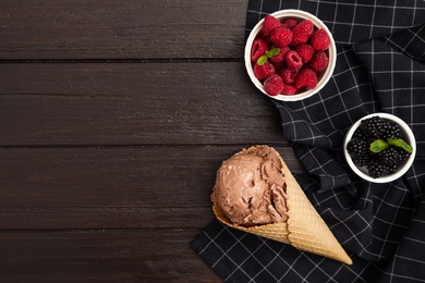 Photo of Delicious chocolate ice cream in wafer cone and different berries on wooden table, flat lay. Space for text
