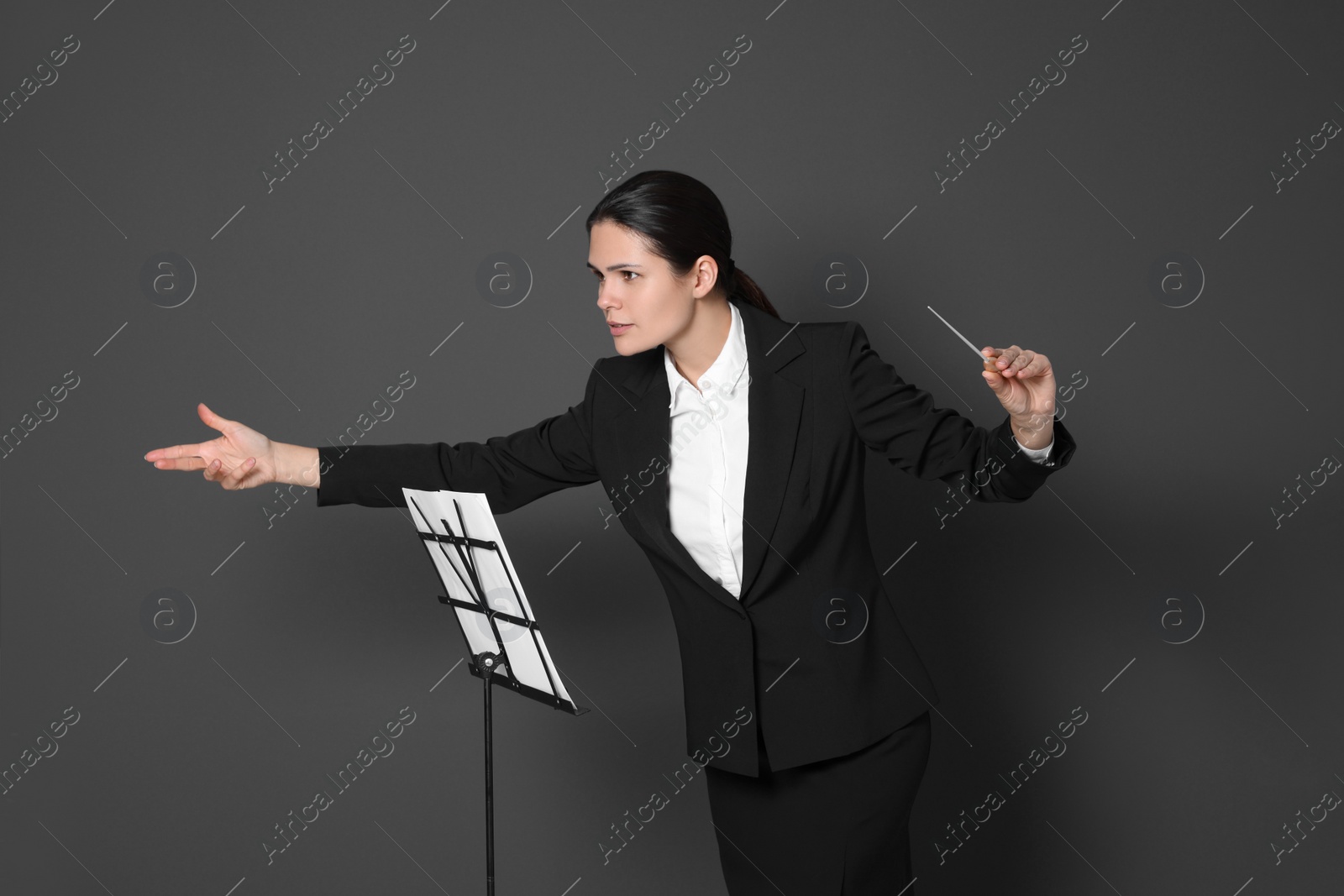 Photo of Happy professional conductor with baton and note stand on grey background