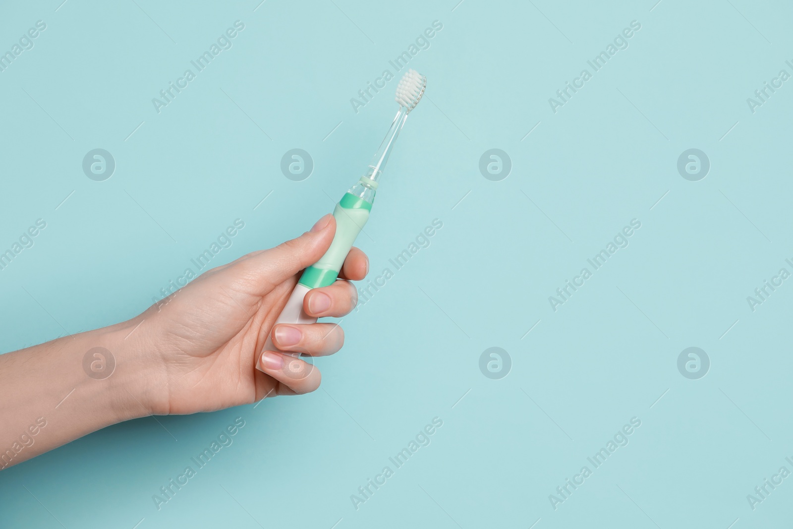 Photo of Woman holding electric toothbrush on light blue background, closeup. Space for text