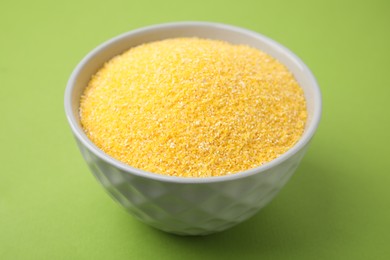 Photo of Raw cornmeal in bowl on green table, closeup