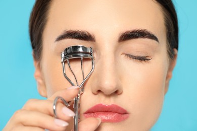 Photo of Woman using eyelash curler on turquoise background, closeup