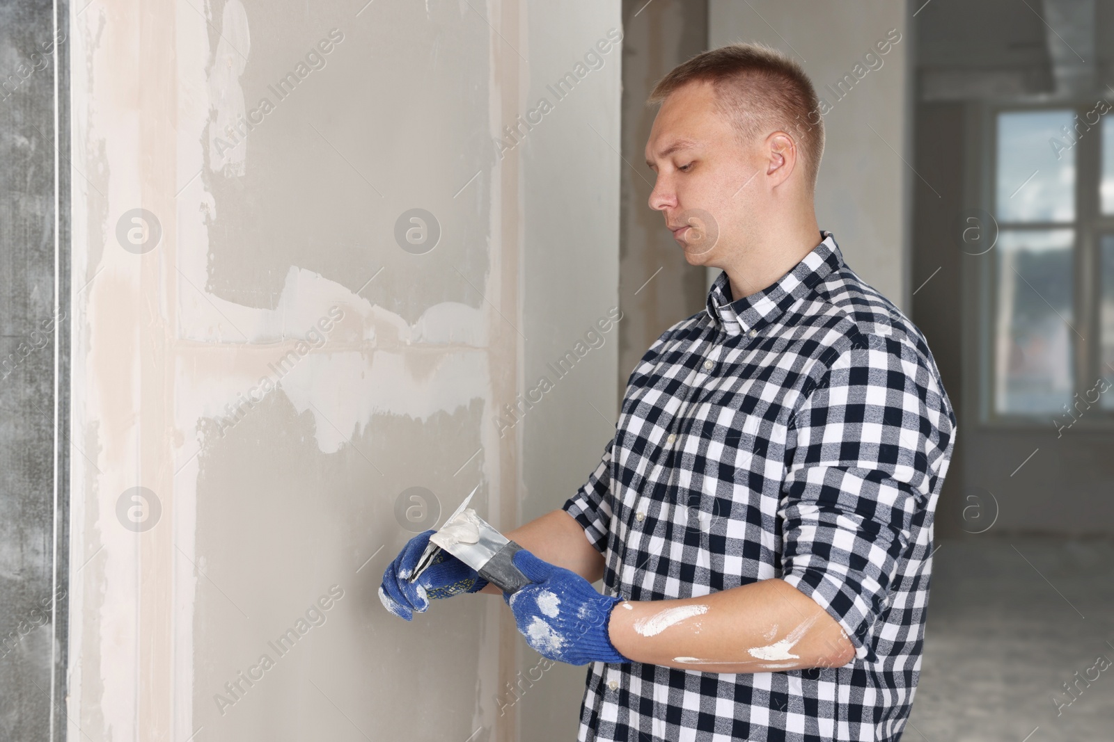 Photo of Worker with putty knives and plaster near wall indoors. Home renovation