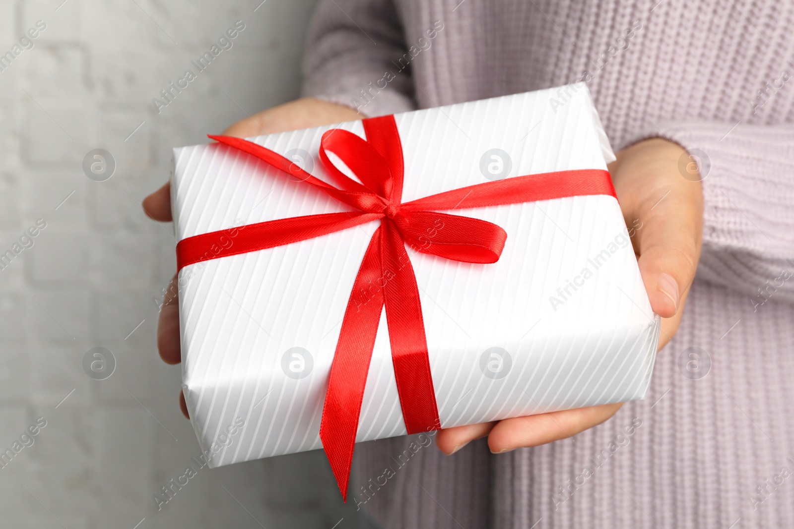 Photo of Young woman holding Christmas gift on light background, closeup