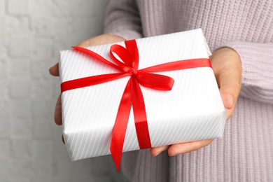 Young woman holding Christmas gift on light background, closeup