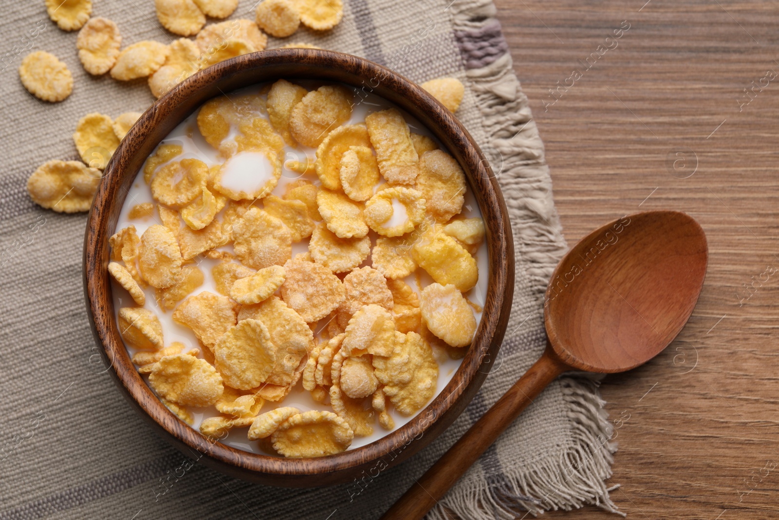 Photo of Tasty cornflakes with milk in bowl served on wooden table, flat lay