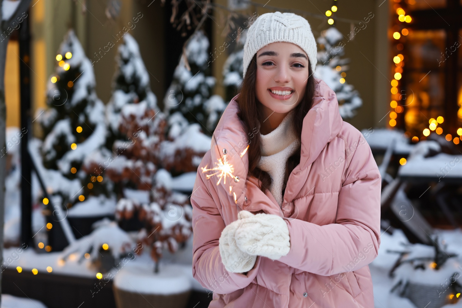 Photo of Portrait of smiling woman with burning sparkle on snowy city street. Space for text