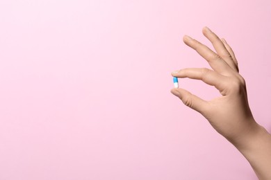 Woman holding pill on pink background, closeup. Space for text