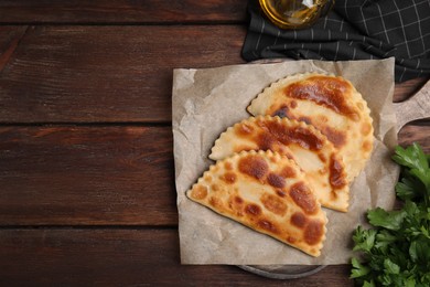 Photo of Board with delicious fried chebureki and parsley on wooden table, flat lay. Space for text