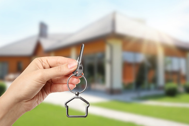 Image of Woman with key near new modern house outdoors, closeup