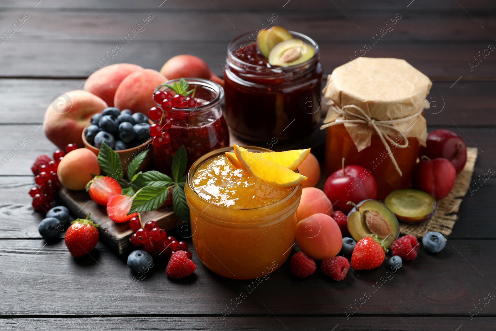 Photo of Jars with different jams and fresh fruits on wooden table