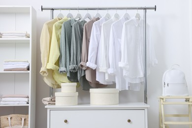 Wardrobe organization. Rack with different stylish clothes, chest of drawers and folding ladder near white wall indoors