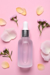 Photo of Bottle of cosmetic serum, flowers and petals on pink background, flat lay