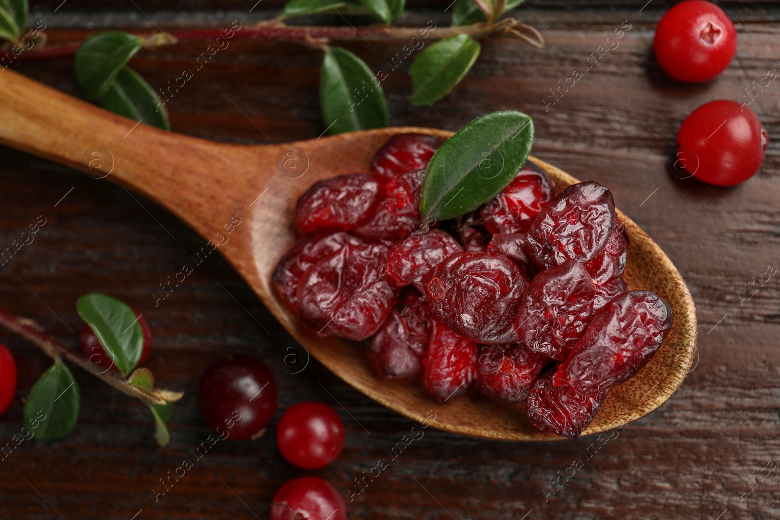 Photo of Tasty dried cranberries in spoon, fresh ones and leaves on wooden table, top view