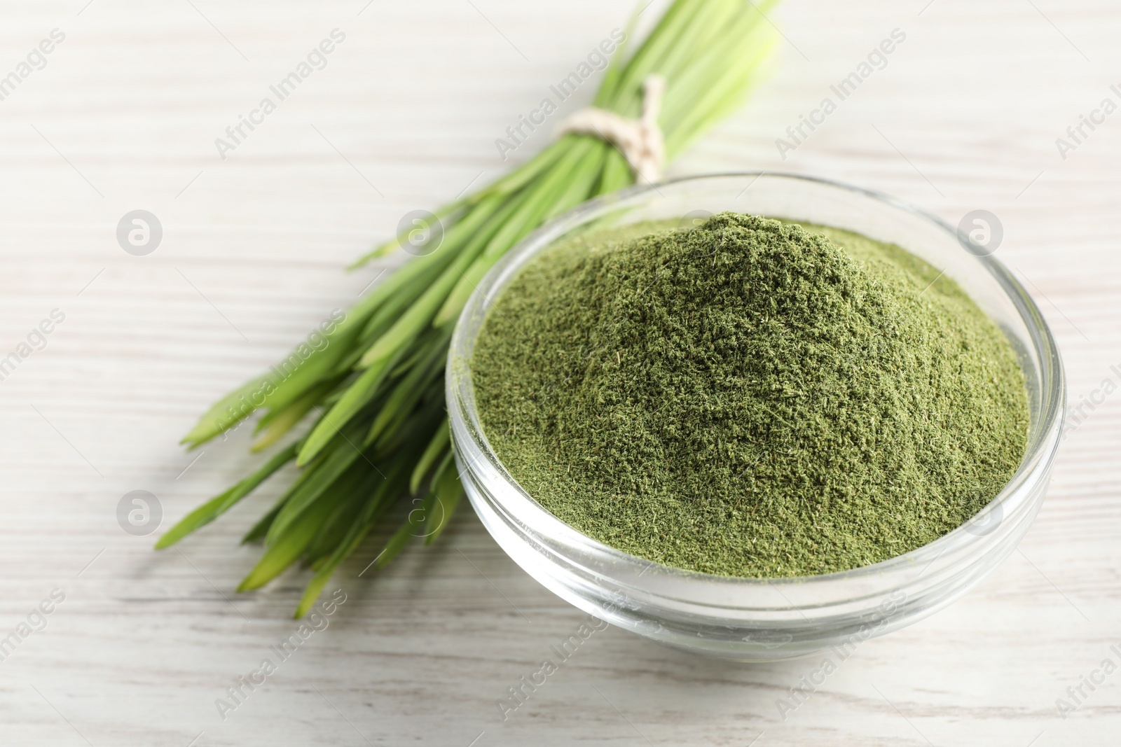 Photo of Wheat grass powder in glass bowl and fresh sprouts on white wooden table, closeup