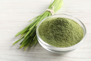 Wheat grass powder in glass bowl and fresh sprouts on white wooden table, closeup