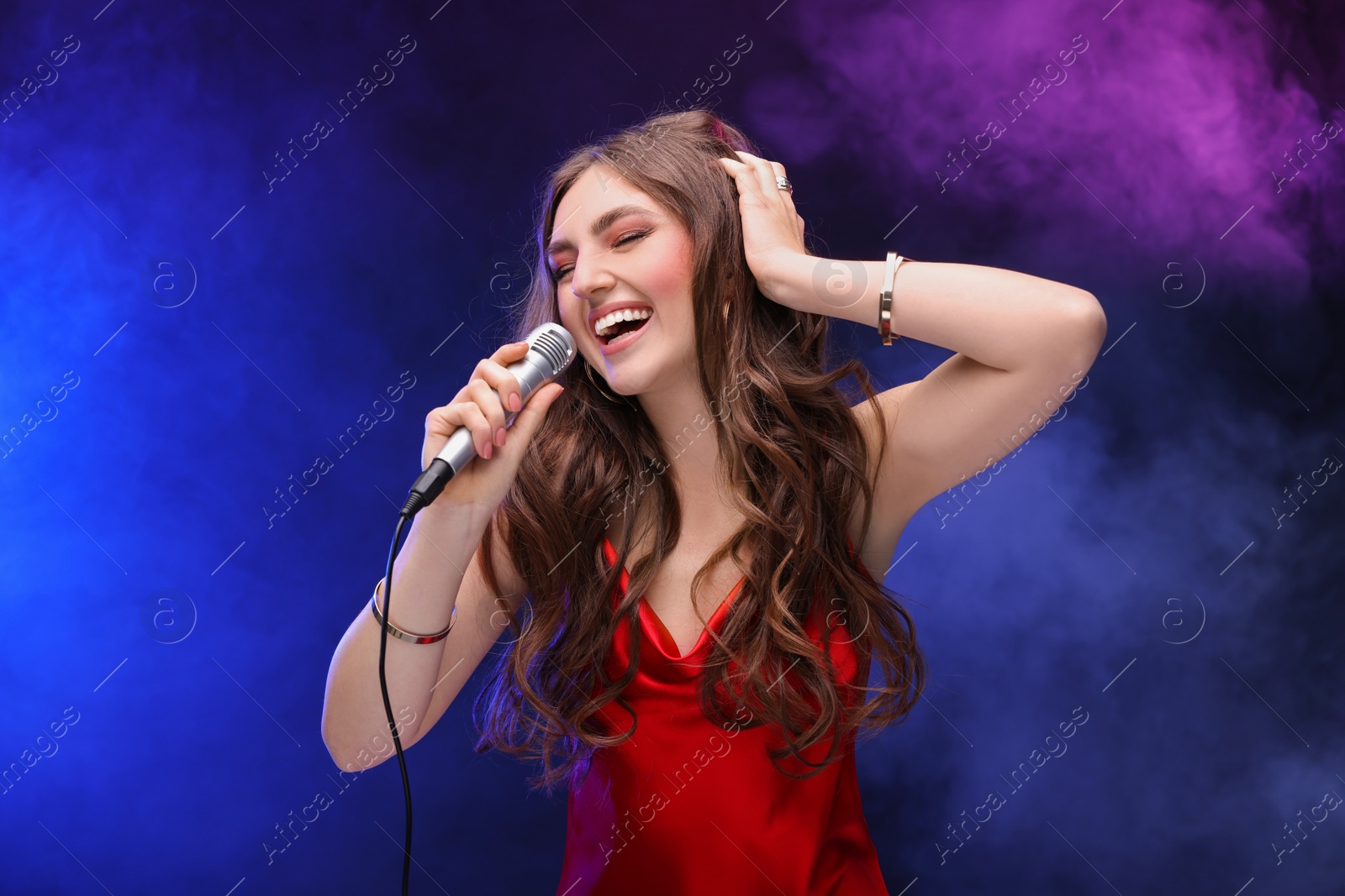 Photo of Beautiful woman with microphone singing in color lights