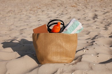Photo of Beach bag with towel, book and sunscreen on sand