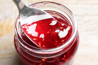 Image of Spoon with strawberry jam in jar on table, closeup