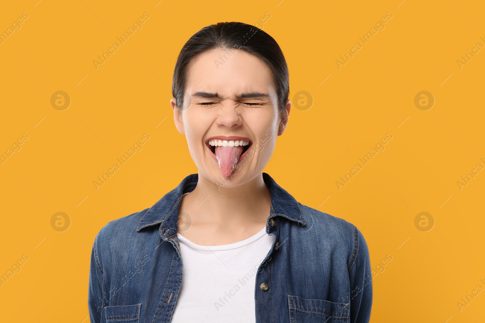 Photo of Happy young woman showing her tongue on yellow background