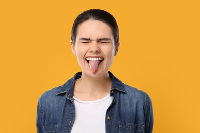 Happy young woman showing her tongue on yellow background
